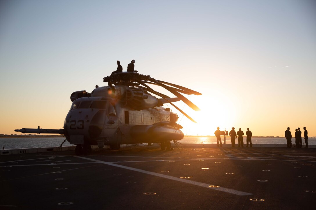 Marines stand on the deck of a ship near a large helicopter.