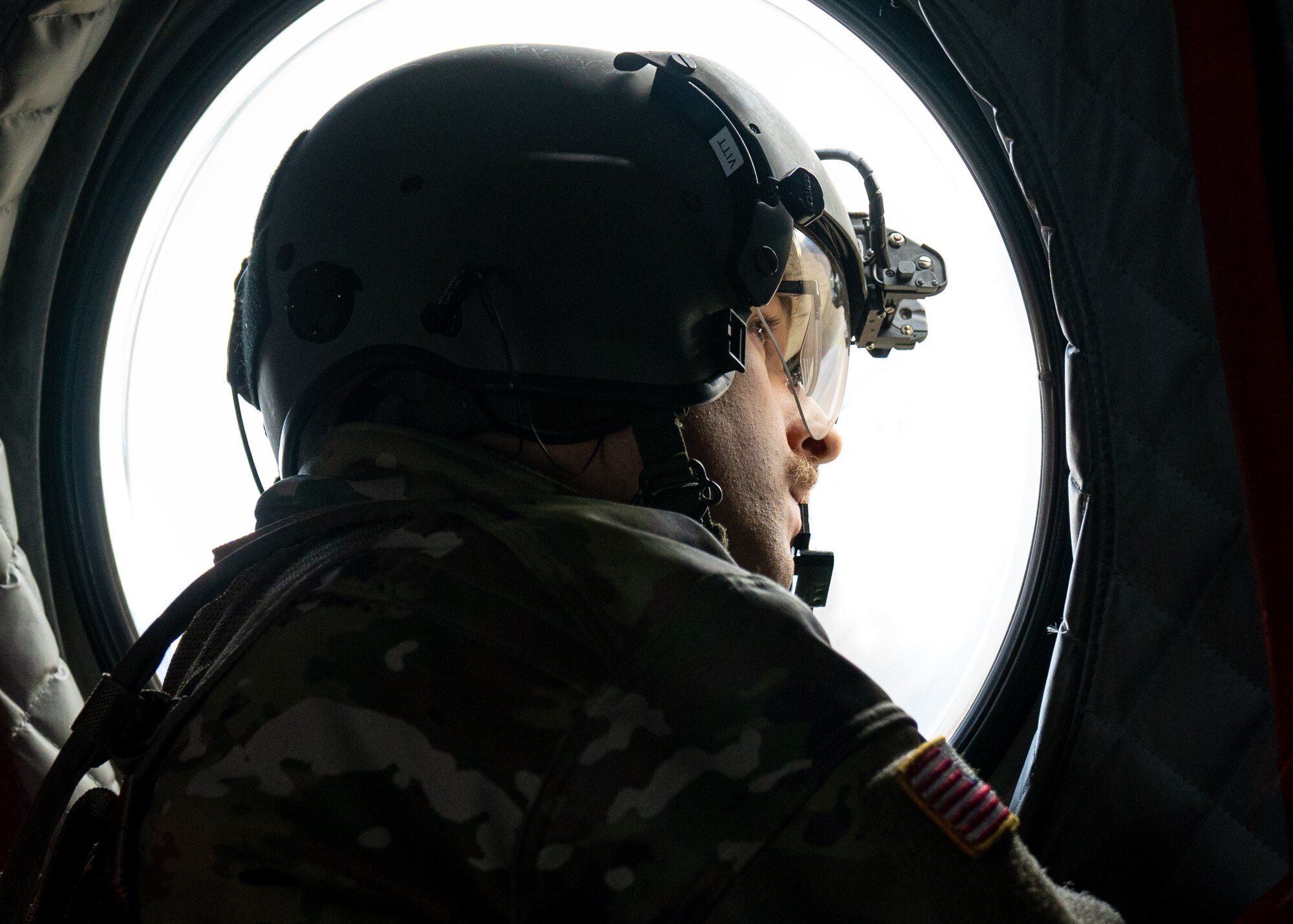 A U.S. Army soldier assigned to Detachment 1, Bravo Company, 2-211th General Service Aviation Battalion, Army National Guard, looks out of the window of a CH-47J Chinook as it transports pararescuemen assigned to the 212th Rescue Squadron, Alaska Air National Guard, back from Malemute Drop Zone during a training event at Joint Base Elmendorf-Richardson.