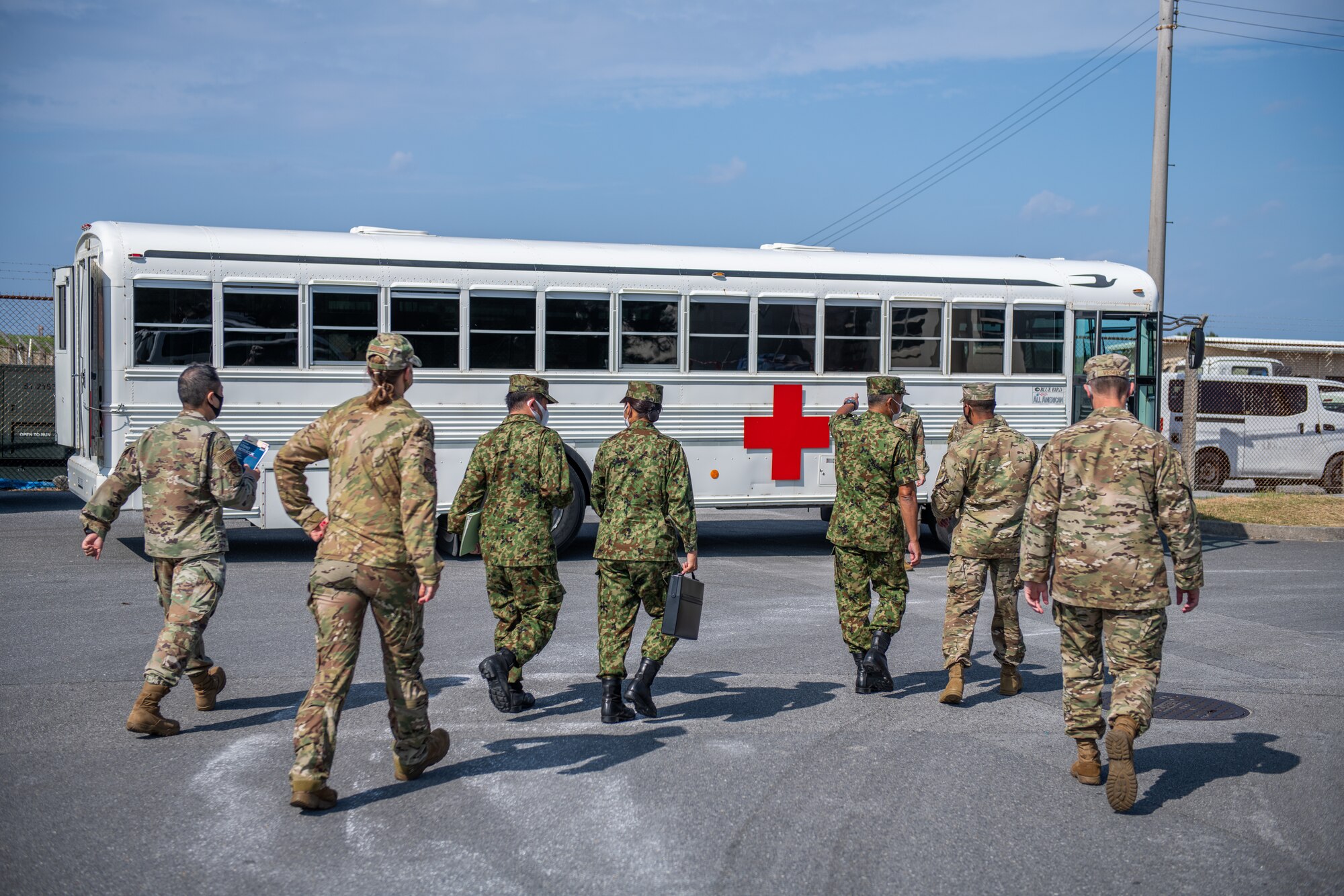 A bunch of American and Japanese military personnel approach a medical bus