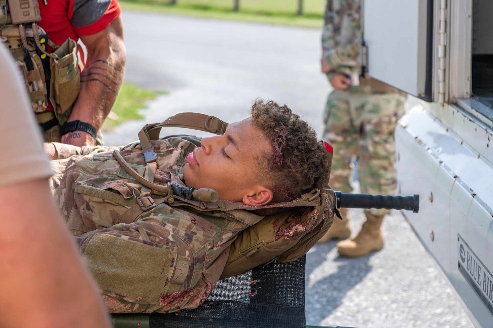An Airman lays on a stretcher as two other military members raise him onto a bus