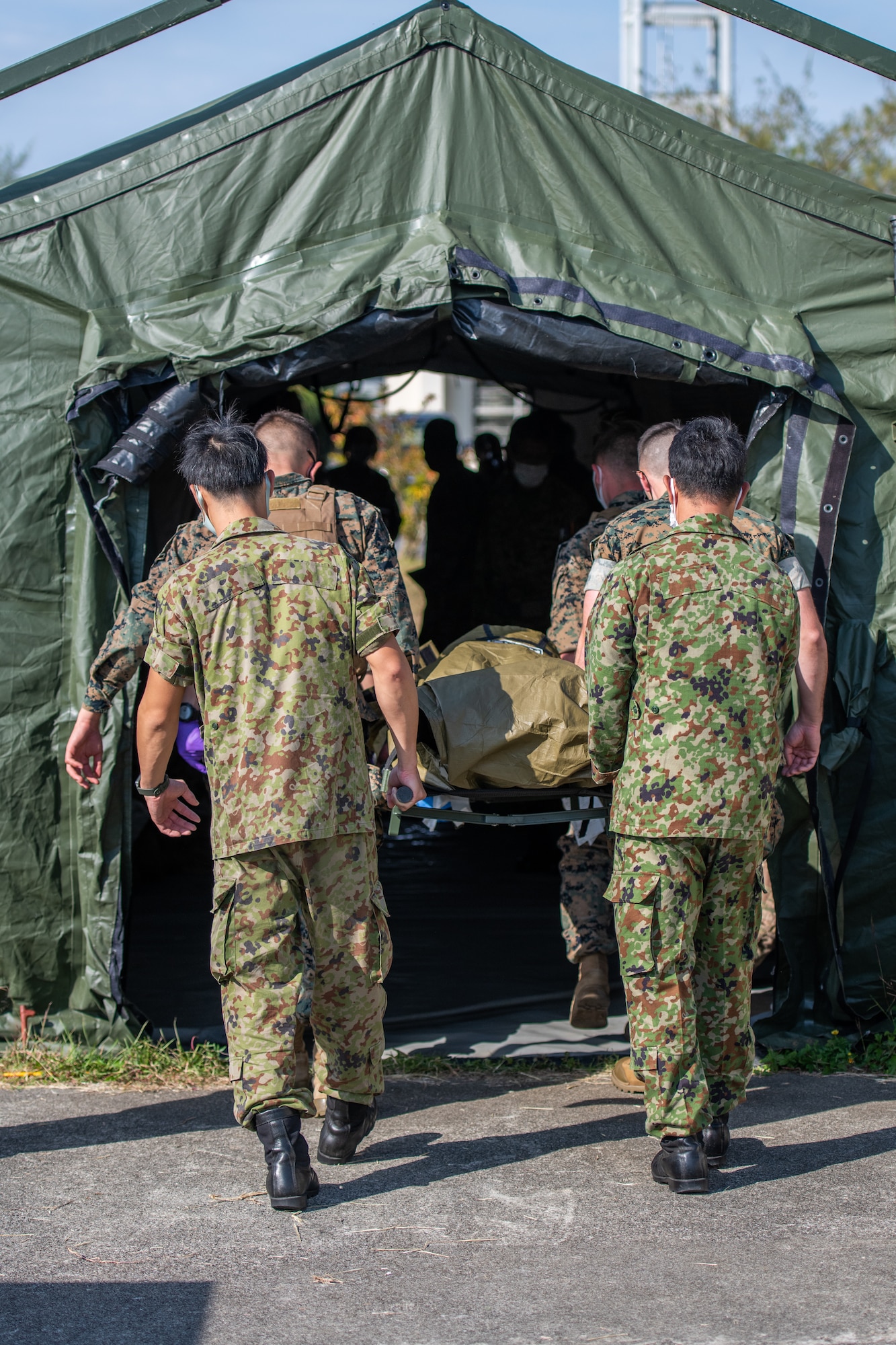 A mix of American and Japanese military members carry a stretcher with a fake patient into a medical tent