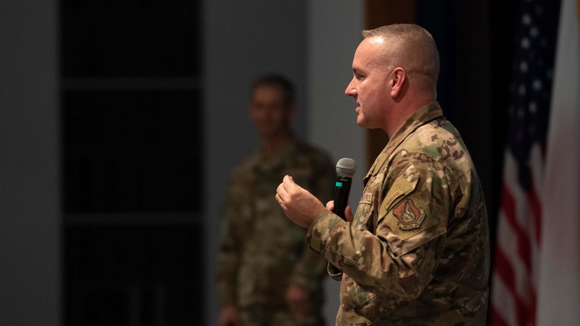 The Pacific Air Forces command chief speaks to a crowd from a stage top.