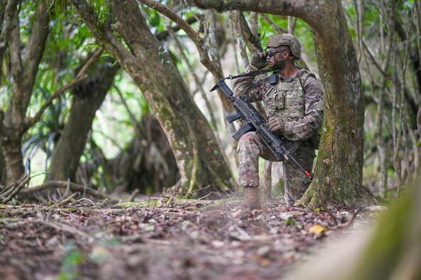 A man kneeling next to a tree looking to the left.