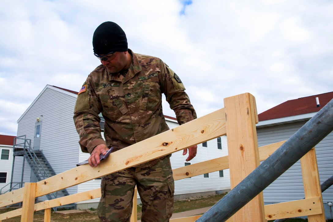 A soldier uses sandpaper to smooth a handrail on a ramp built for Afghan personnel.