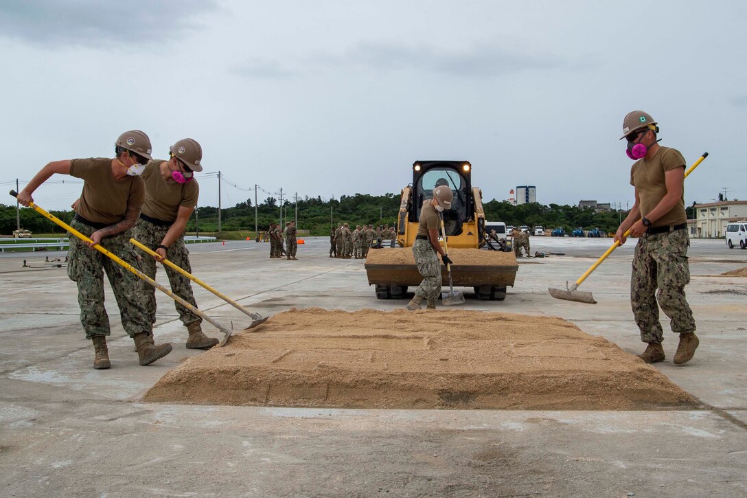 Service members use tools to smooth sand on an airfield.