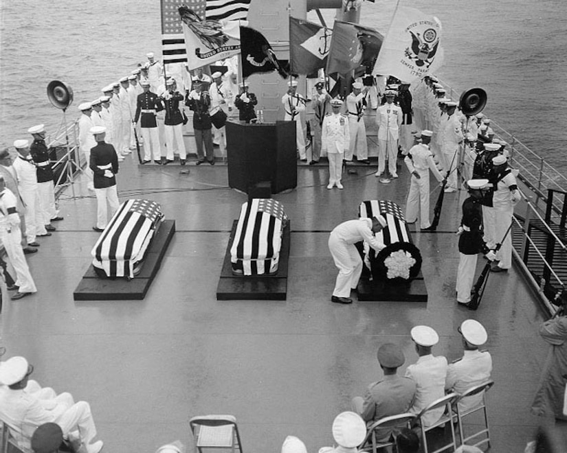 Sailors on ship look at three caskets.