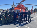 Coast Guard service members gather with a Coast Guard veteran in front of a helicopter to celebrate his 100th birthday