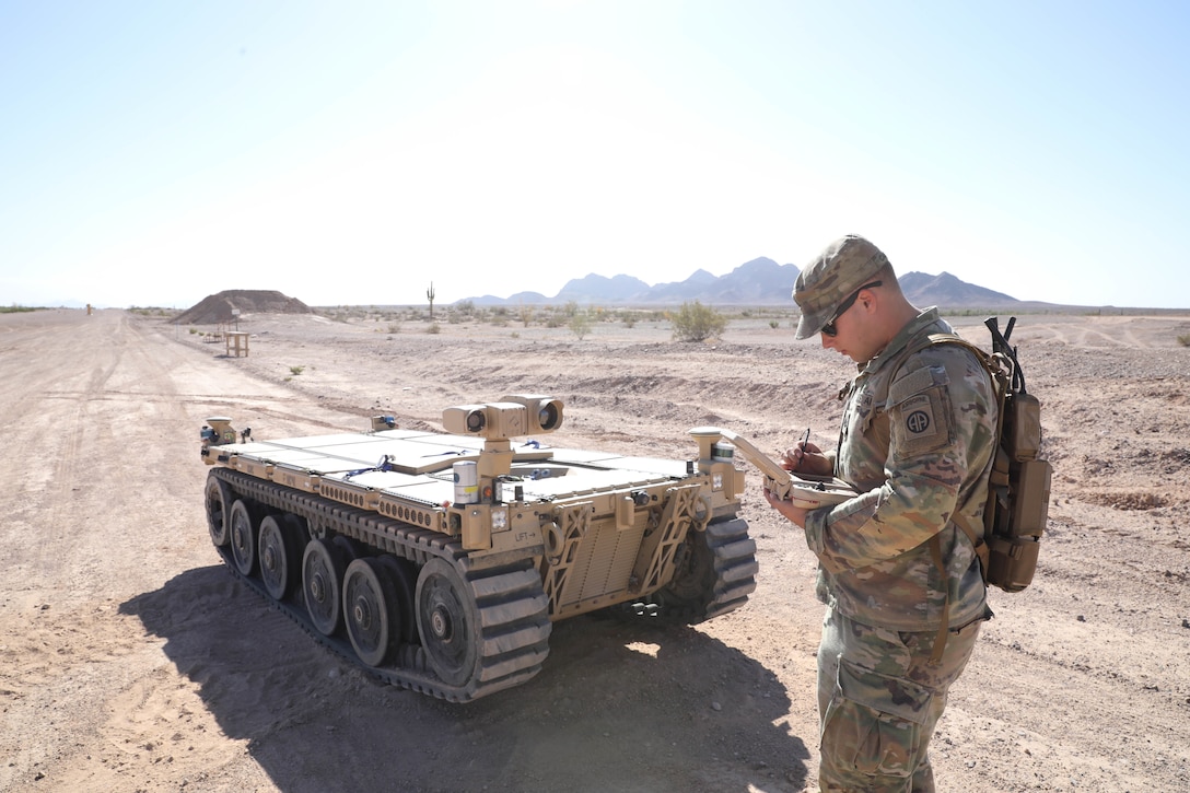 A man holds a device while standing in front of robotic vehicle.
