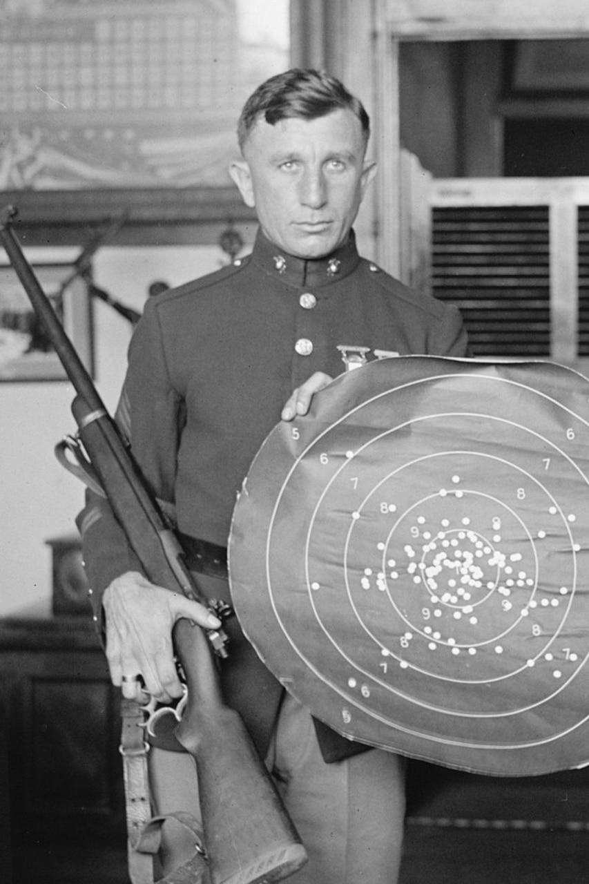 A Marine holds a rifle and target.