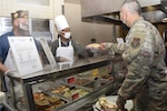 Andrew Camplen, 433rd AW honorary commander, and Col. Nikhil Patel, 433rd Airlift Wing vice commander, serve food to an Air Force service member at the Live Oak Dining Facility Nov. 6, 2021, on Joint Base San Antonio-Lackland, Texas. The “Serve our Airmen” event allowed honorary commanders to connect with military service members to help foster community relations. (U.S. Air Force photo by Senior Airman Brittany Wich)