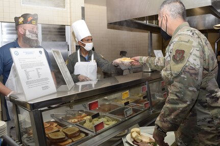 Andrew Camplen, 433rd AW honorary commander, and Col. Nikhil Patel, 433rd Airlift Wing vice commander, serve food to an Air Force service member at the Live Oak Dining Facility Nov. 6, 2021, on Joint Base San Antonio-Lackland, Texas. The “Serve our Airmen” event allowed honorary commanders to connect with military service members to help foster community relations. (U.S. Air Force photo by Senior Airman Brittany Wich)