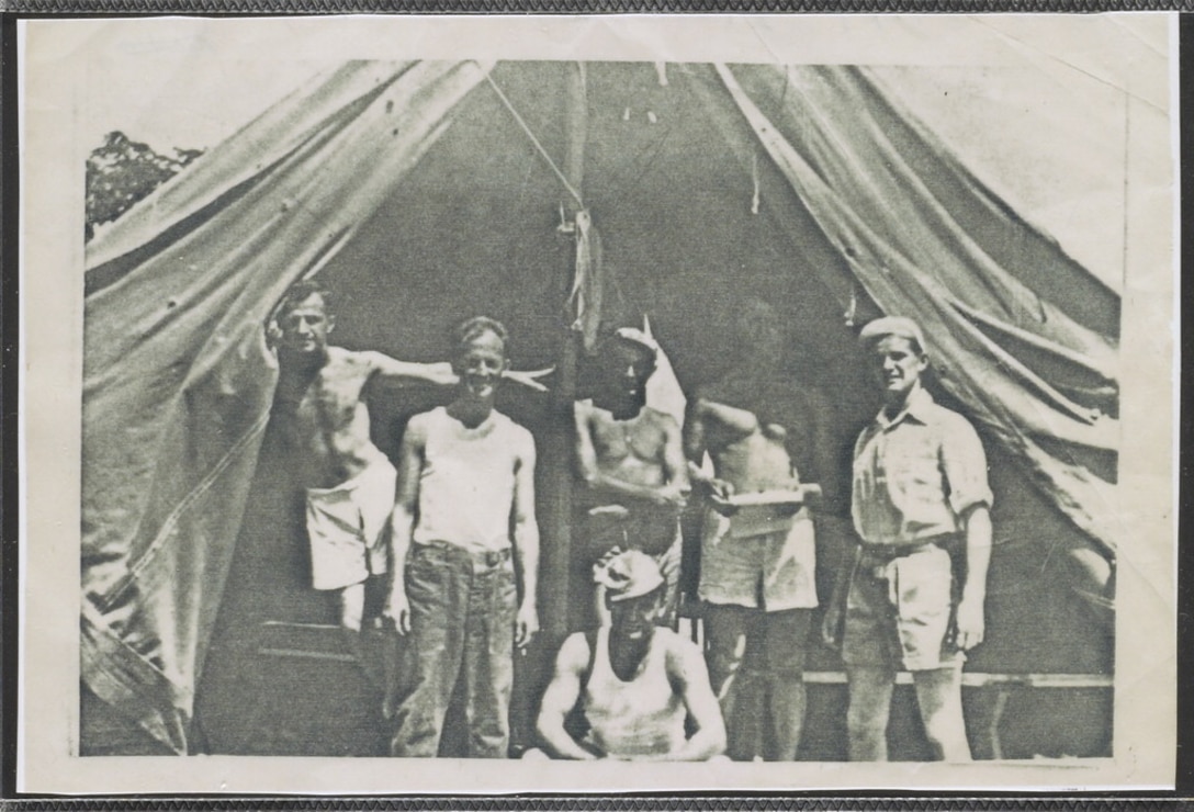 Six men stand inside a tent.