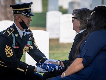 The Noncommissioned Officer in Charge of the casket team presents the flag to Katherine C. Gandara, niece of Army Cpl. Norvin D. Brockett during his burial at Arlington National Cemetery on July 21, 2021.