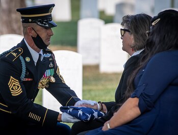 The Noncommissioned Officer in Charge of the casket team presents the flag to Katherine C. Gandara, niece of Army Cpl. Norvin D. Brockett during his burial at Arlington National Cemetery on July 21, 2021.