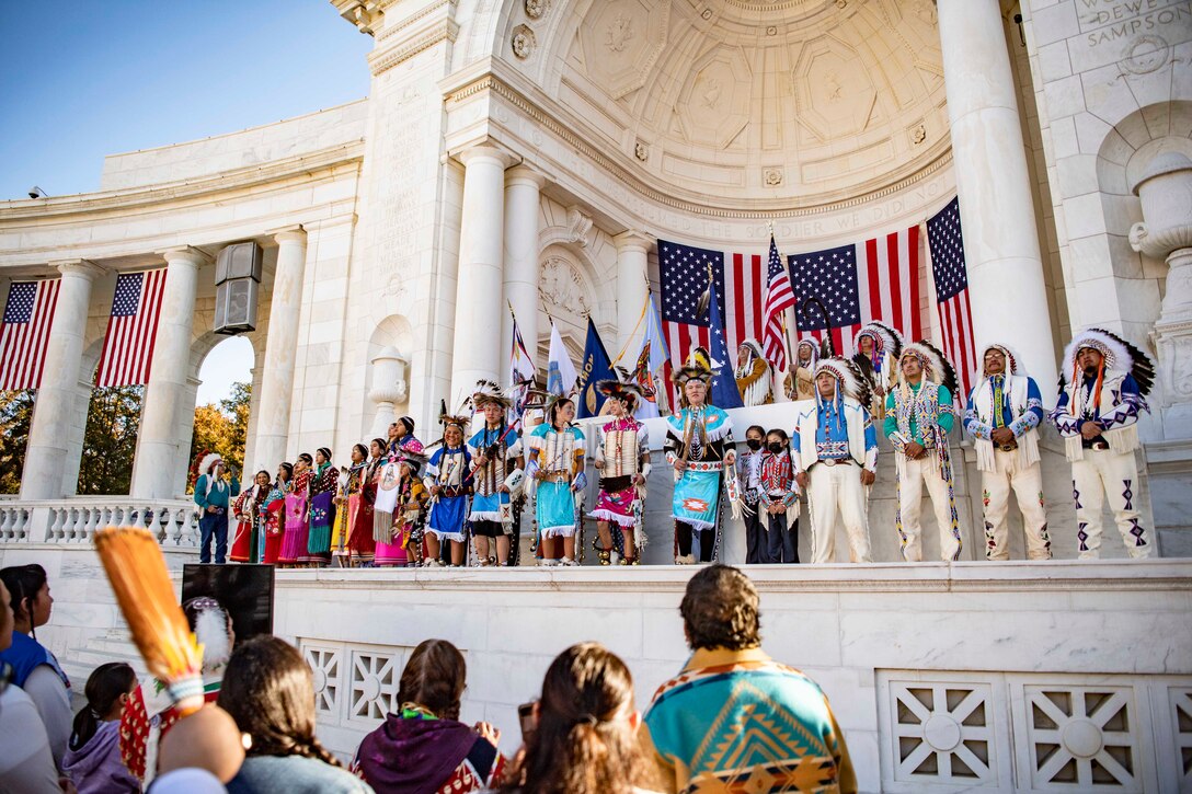 Members of the Crow Nation perform on a stage for a crowd below.