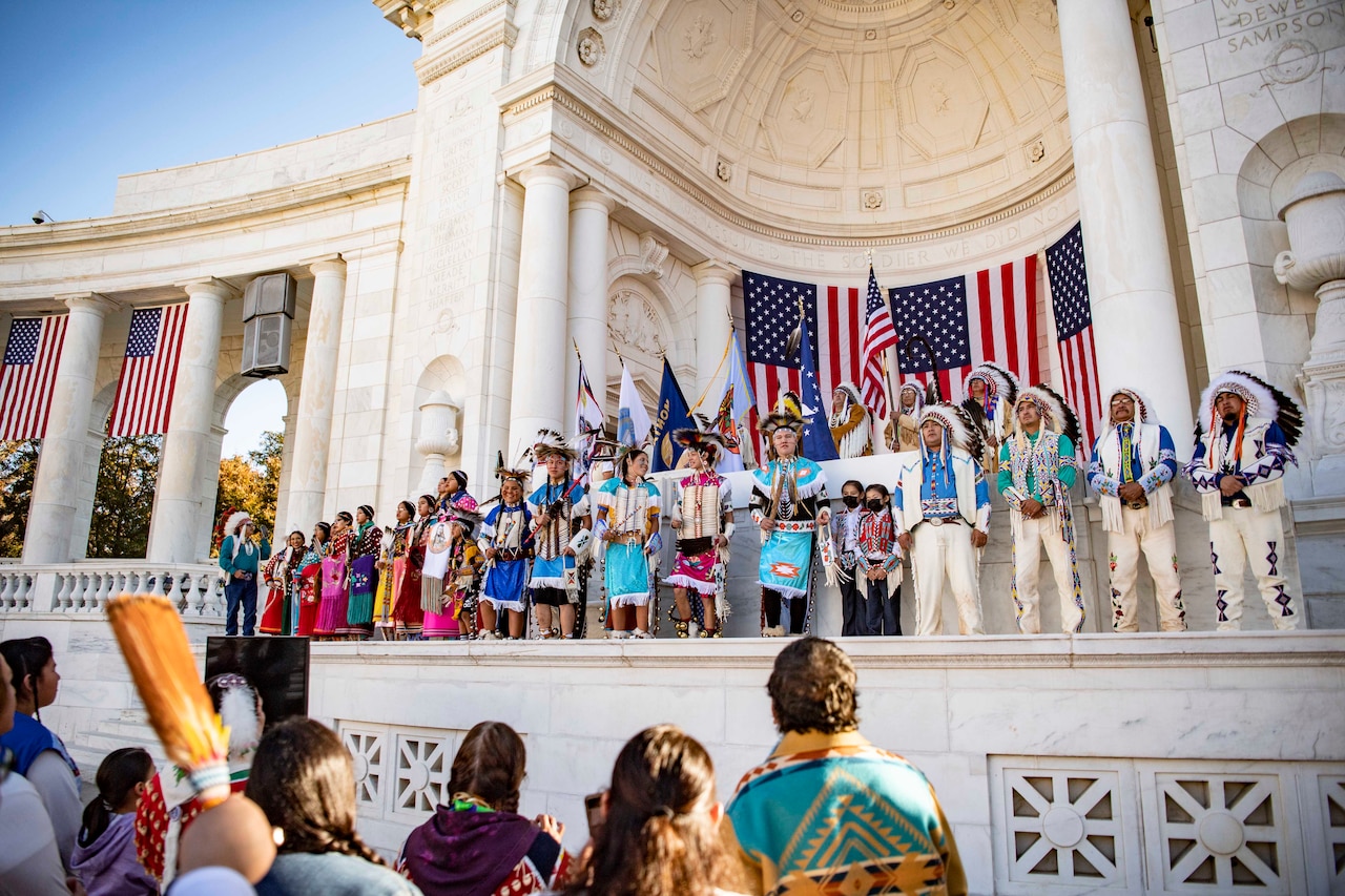 Members of the Crow Nation perform on a stage for a crowd below.