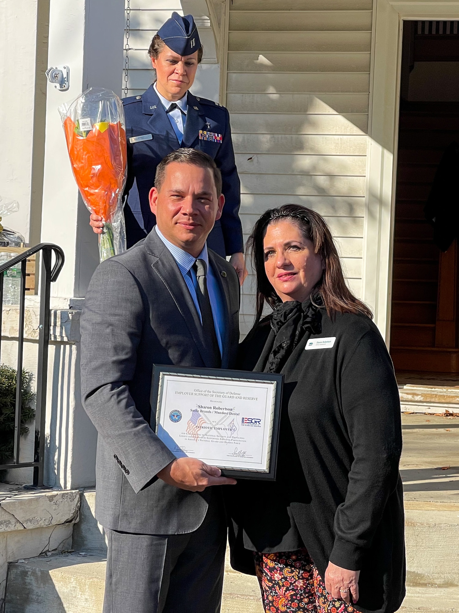 McMahon stands next to Robertson holding the Patriot Award certificate. Hartsell stands in background holding a bouquet of flowers.
