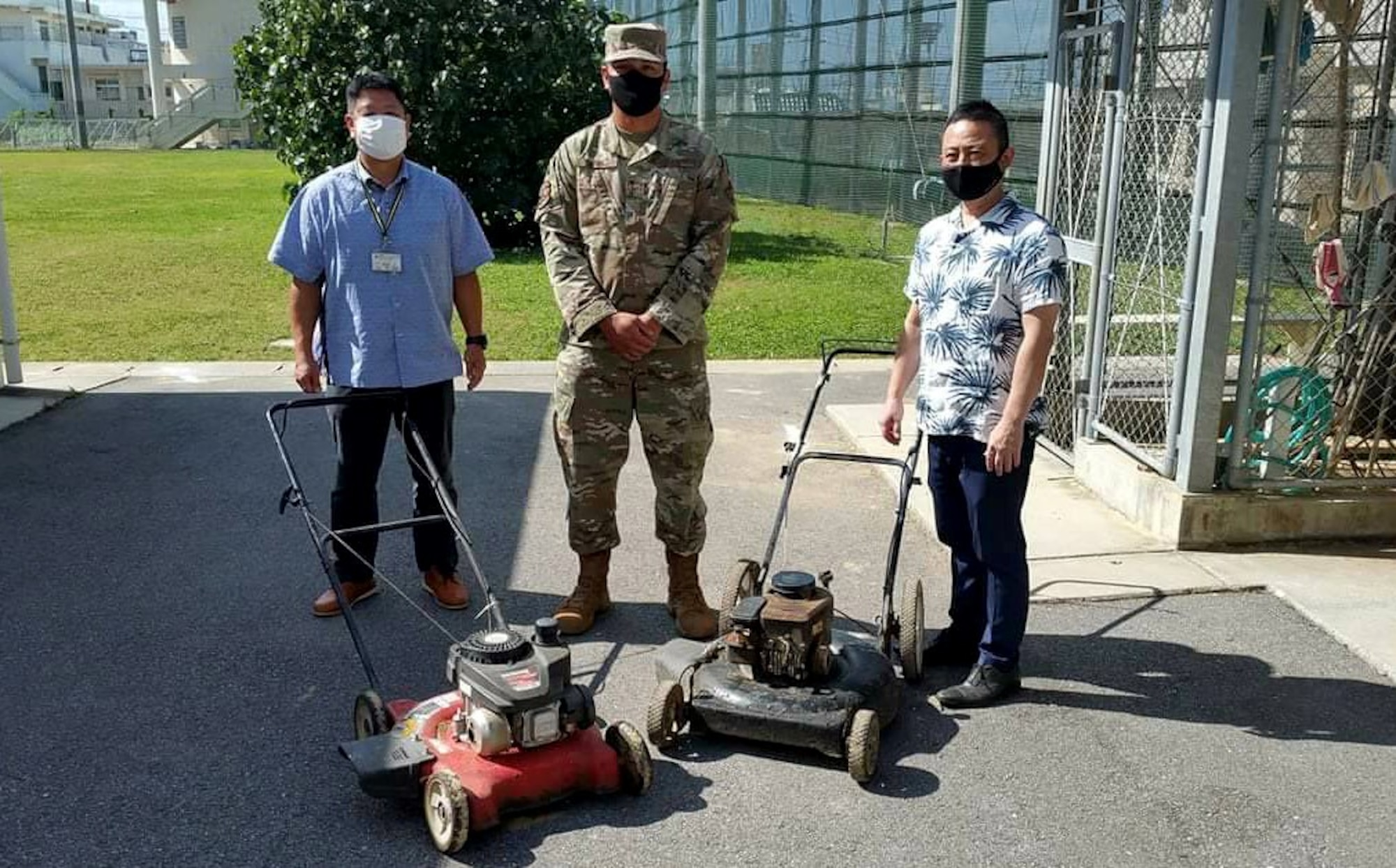 Three men stand behind two lawnmowers.