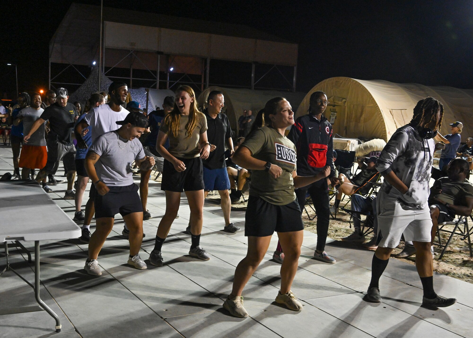 Personnel deployed to Prince Sultan Air Base line-dance during a DJ set performed by U.S. Air Force Tech. Sgt. Kelcey McDonald, U.S. Air Forces Central Band audio engineer, during a concert at PSAB, Kingdom of Saudi Arabia, Oct. 16, 2021. The 378th Air Expeditionary Wing hosted two nights of performances in recognition and celebration of the base’s accomplishments throughout the past summer. (U.S. Air Force photo by Capt. Rachel Buitrago)