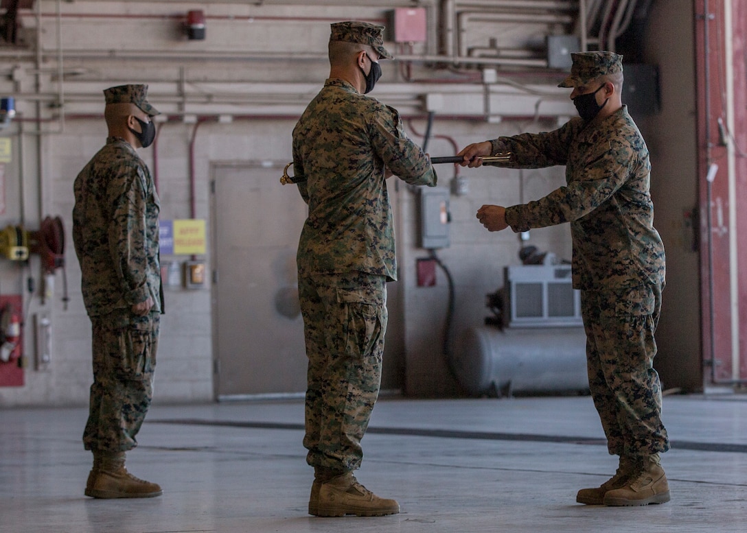 U.S. Marine Corps Sgt. Maj. Hector A. Hernandez (right), oncoming sergeant major, Headquarters and Headquarters Squadron (H&HS), receives the non-commissioned officer (NCO) sword from the Squadron's commanding officer, Lt. Col. Robert G. Reinoehl (center), at Marine Corps Air Station (MCAS) Yuma, Ariz., Nov. 9, 2021. As Reinoehl presents the NCO sword to Hernandez, he becomes the appointed sergeant major for H&HS. (U.S. Marine Corps photo by Sgt. Jason Monty)