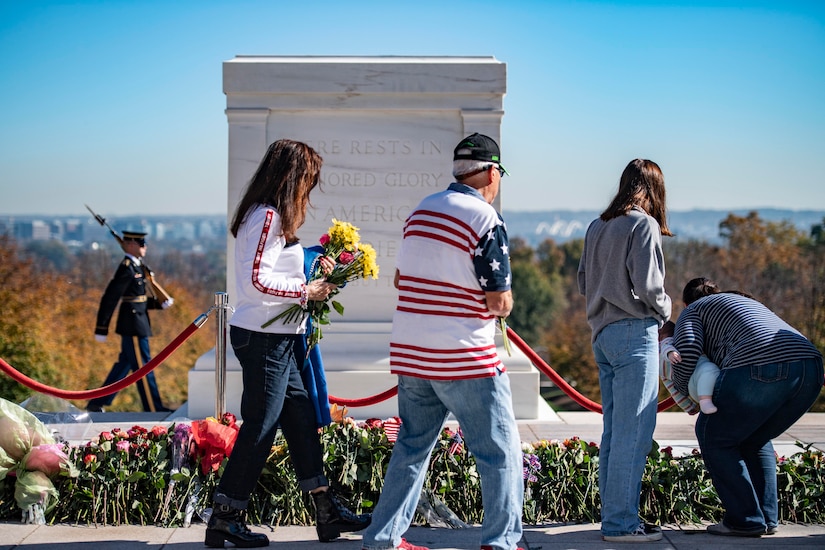 A group of people place flowers in front of a monument.