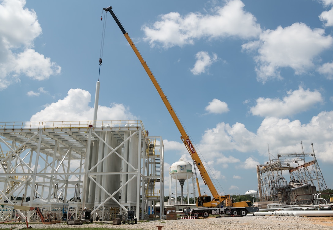 A high-pressure air bottle is lifted and lowered into place in the J-5 test facility bottle farm, Aug. 26, 2021, at Arnold Air Force Base, Tenn. In the background at right, is the J-4 Rocket Engine Test Cell, which is currently inactive. (U.S. Air Force photo by Jill Pickett)