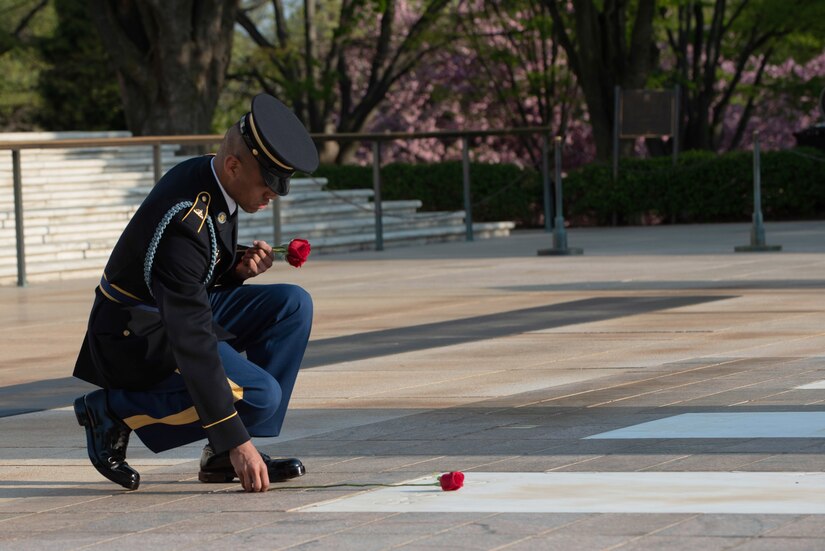 A soldier kneels and places a rose at a crypt at the Tomb of the Unknown Soldier.