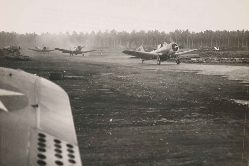 Three World War II-era airplanes taxi down a runway on an island.