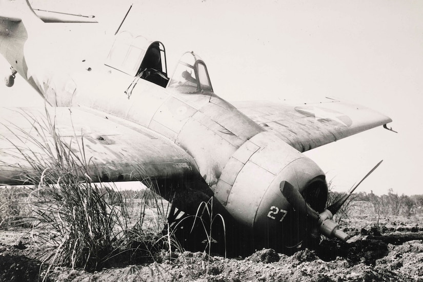 A World War II-era airplane's nose is pushed into dirt. It's tale is up in the air.