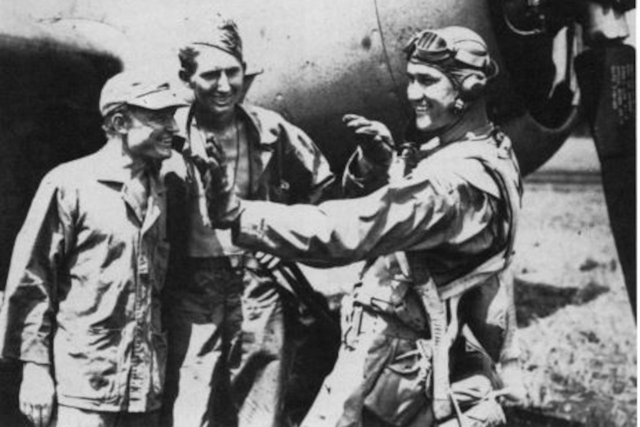 A pilot uses his hands to explain something to two other men beside an airplane.