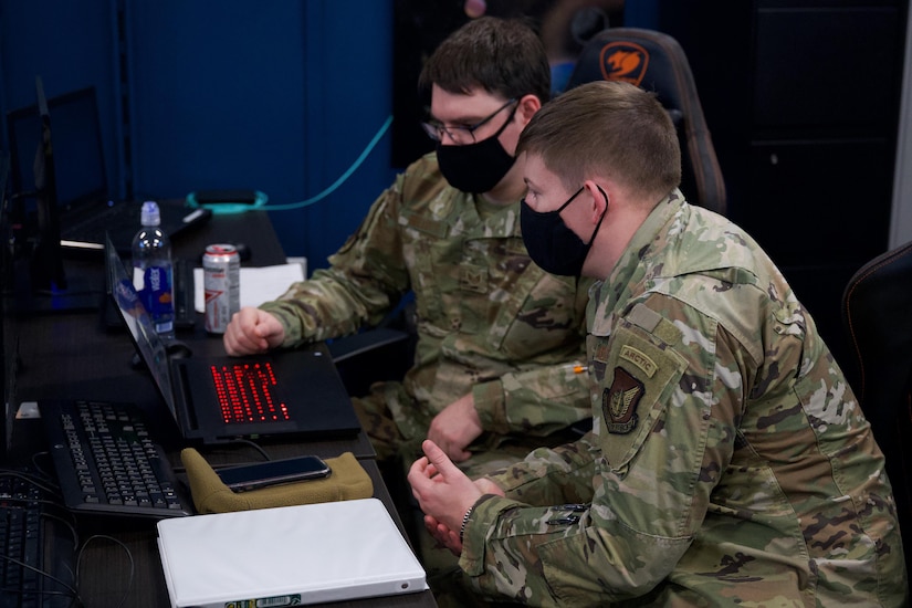 Airmen gather around a laptop.