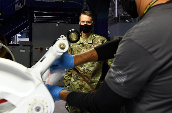 Photo shows hands working on an aircraft part with general watching.