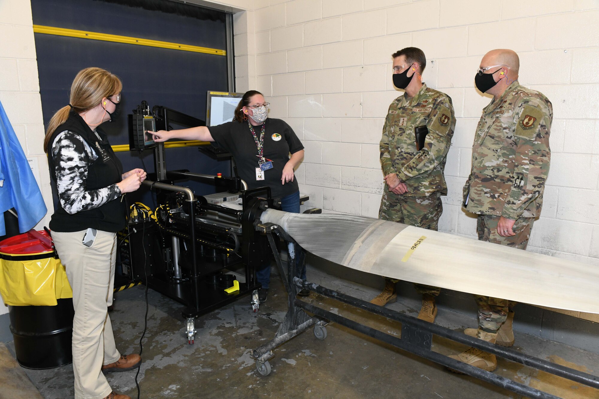 Photo shows people standing around machine holding a propeller blade.