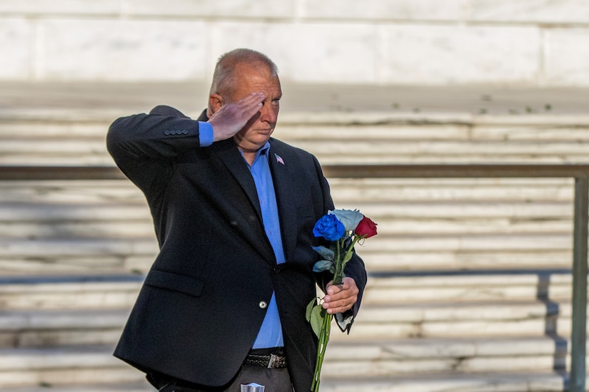 A person salutes and holds flowers at Tomb of the Unknown Soldier.