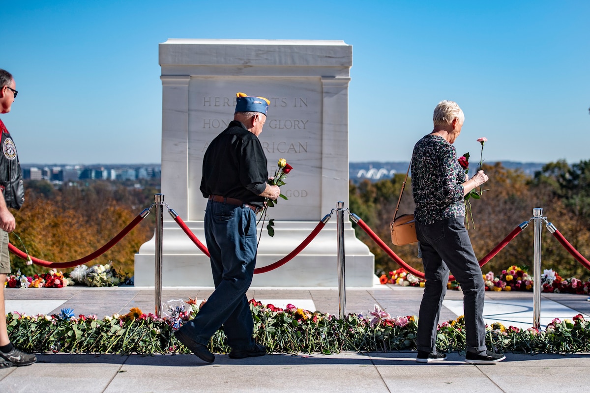 People walk in front of Tomb of the Unknown soldiers with flowers in hand.