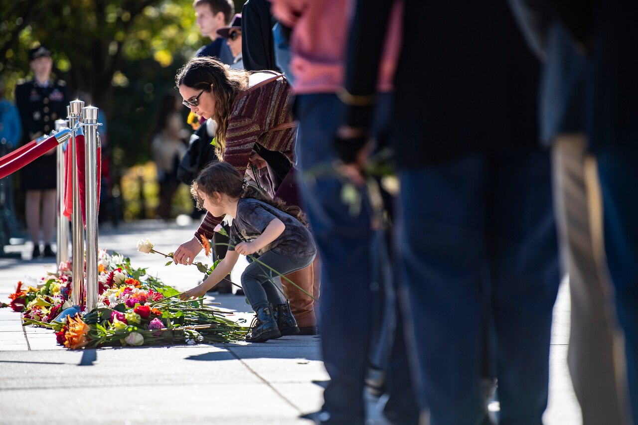 A child and adult place flowers at the Tomb of the Unknown soldier as people wait in line by them.