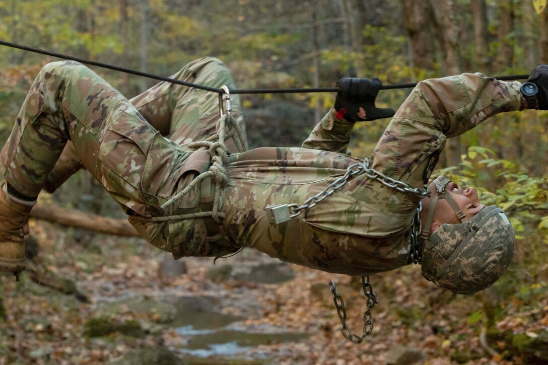 An Army cadet hangs on to rope to climb across a creek in the woods.