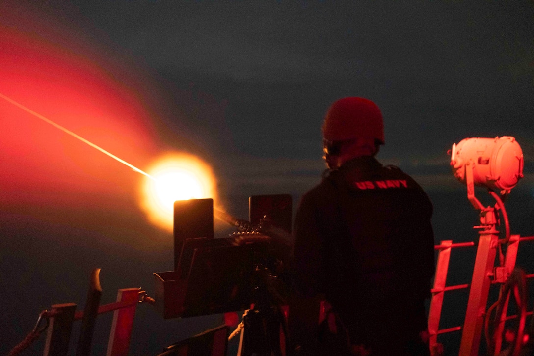 A sailor fires flares from a ship at sea illuminated by red light.