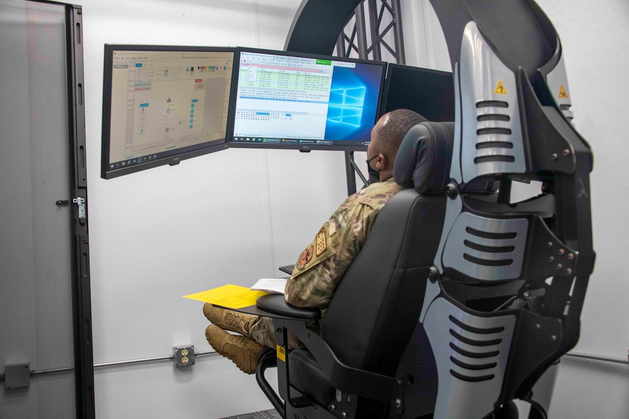 An airman looks at computer screens while seated in a large mechanical chair.