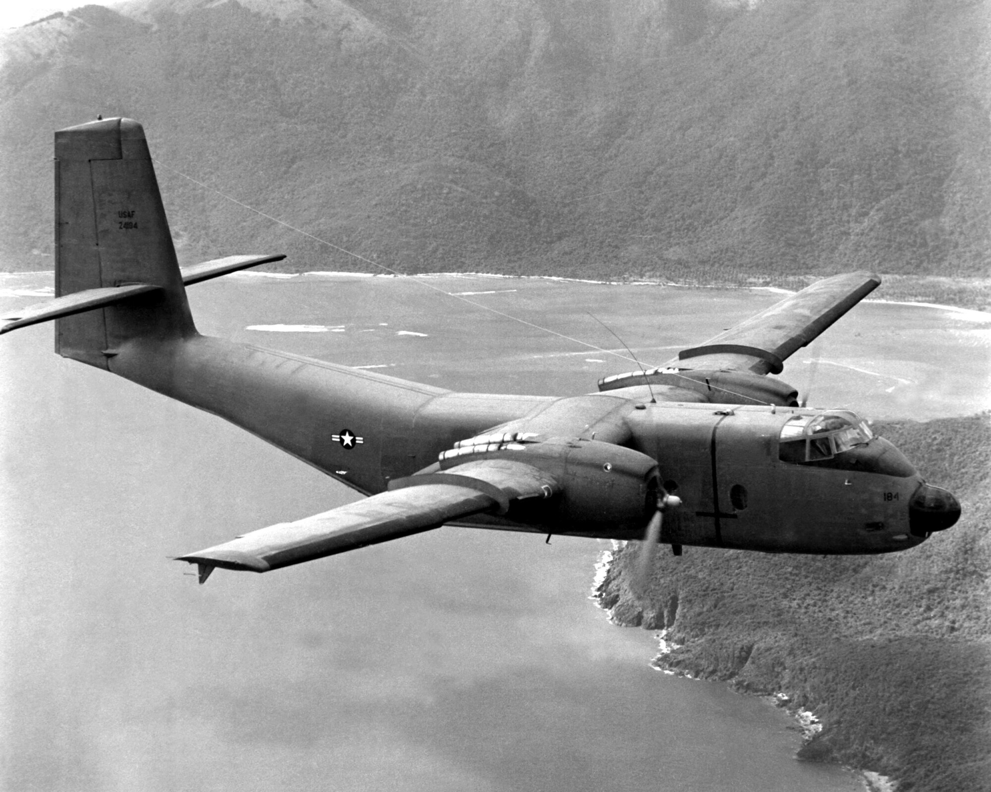 A black and white image of an old military aircraft flying over mountains.