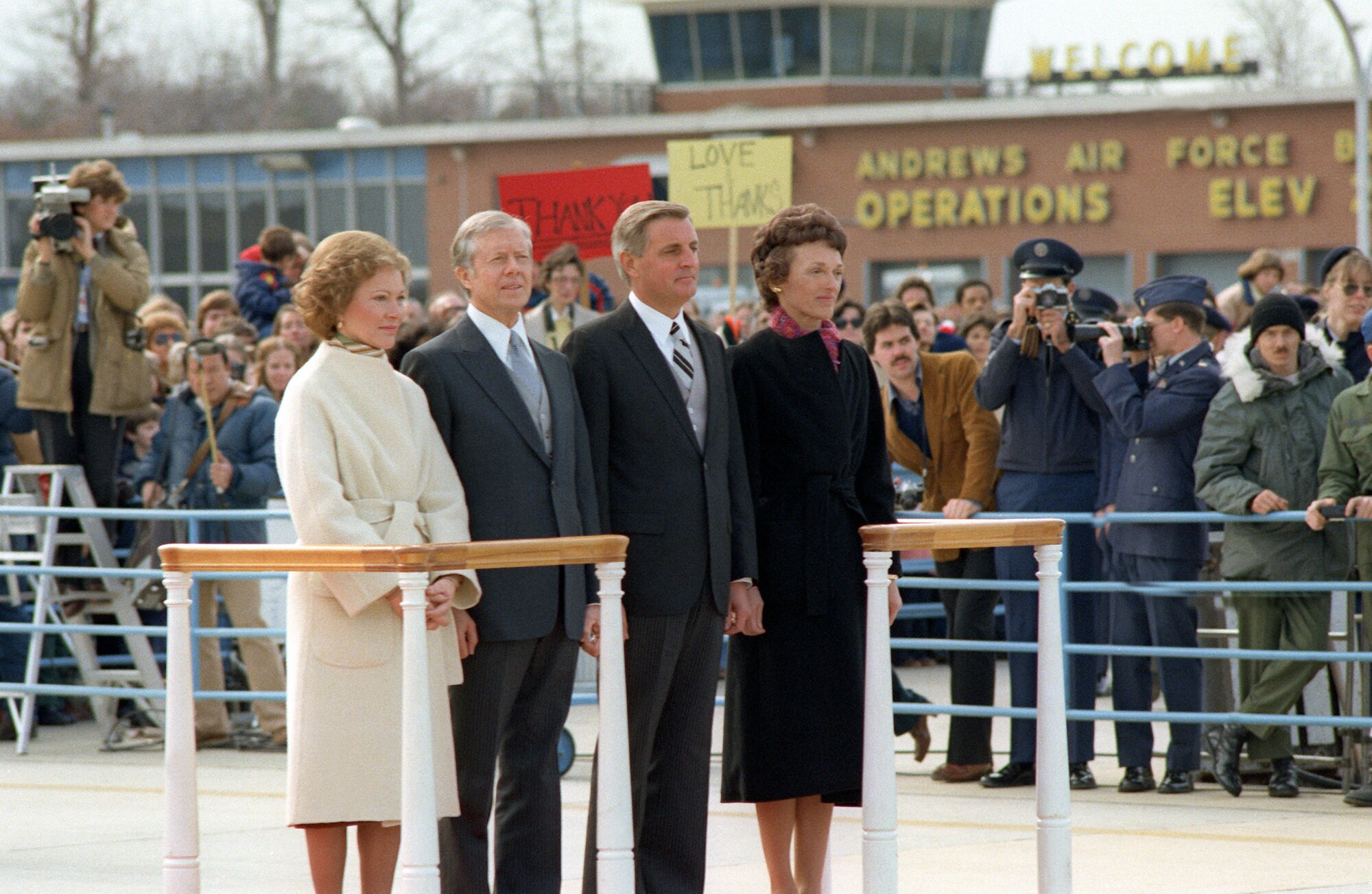Former President and his wife stands with a former vice president and his wife on the flight line with a crowd of people surrounding them.