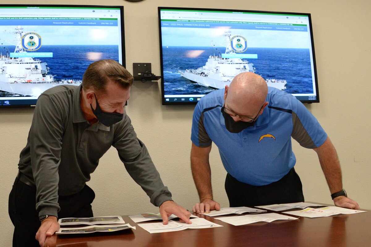 Men wearing masks look over paperwork.