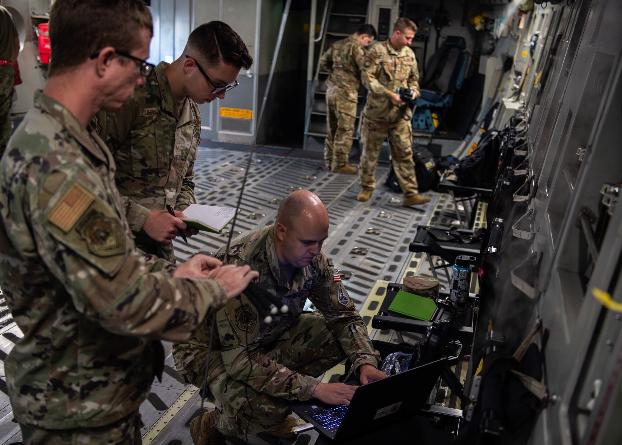 Tech. Sgt. Carl Williams, 747th Cyberspace Squadron standards and evaluations craftsman, Senior Airman Allan Larson and Space Force Specialist 4 Nathan Hall, 747th CYS mission defense team operators, set up connections to a stand-alone hub activity reconnaissance kit in a C-17 Globemaster III at Joint Base Pearl Harbor-Hickam, Hawaii, Nov. 3, 2021. The “SHARK” kit, was developed by members of the 747th CYS to monitor radio frequency abnormalities in-flight. (U.S. Air Force photo by Staff Sgt. Alan Ricker)