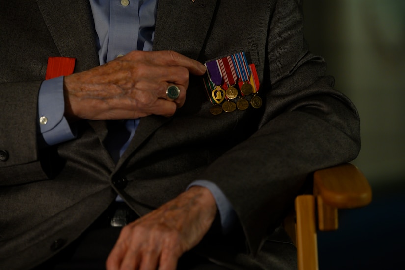 A man's hand points to medals pinned to his suit.