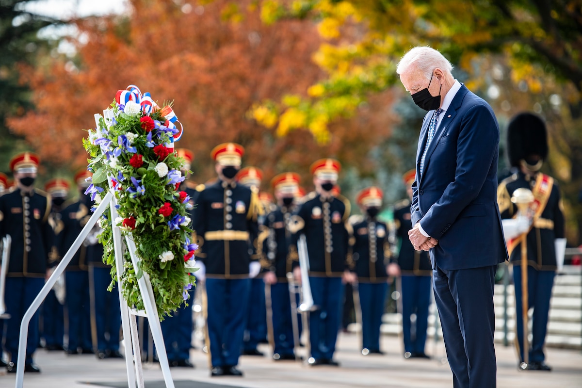 President Joe Biden stares at a wreath near service members at ceremony.