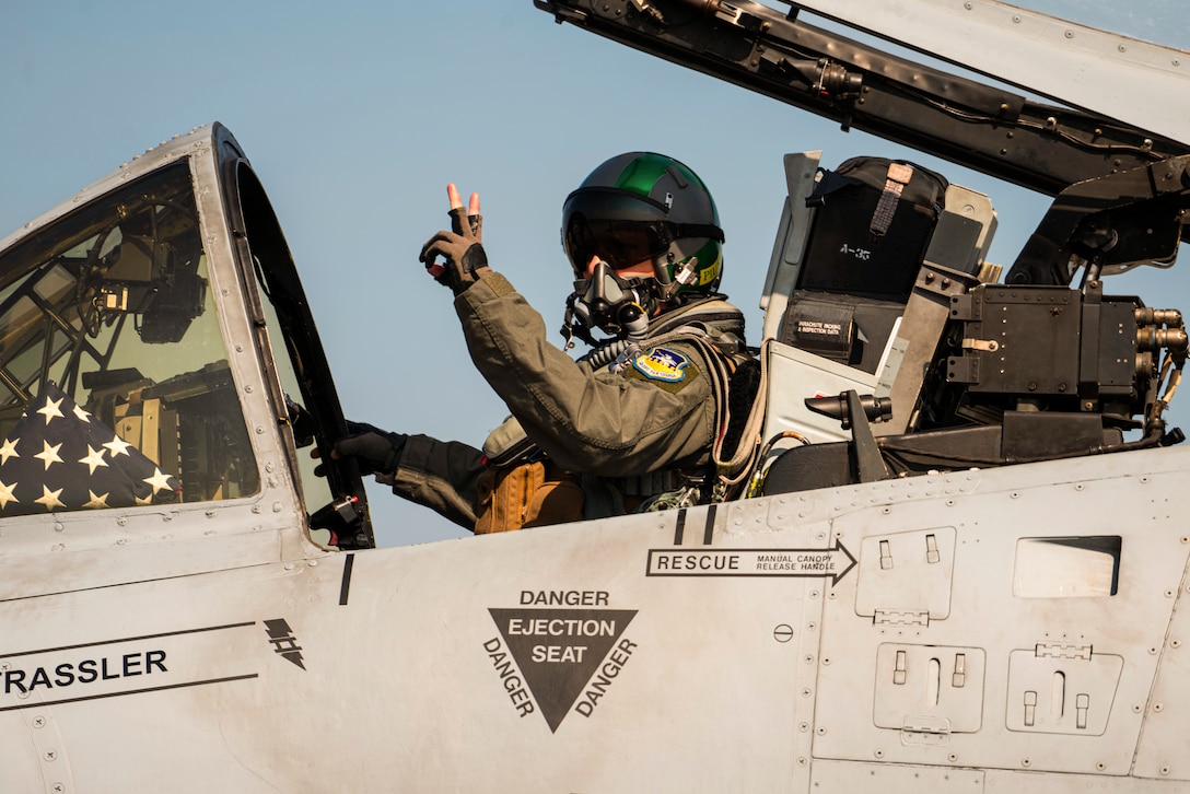 An airman gives the peace sign while sitting in an aircraft.