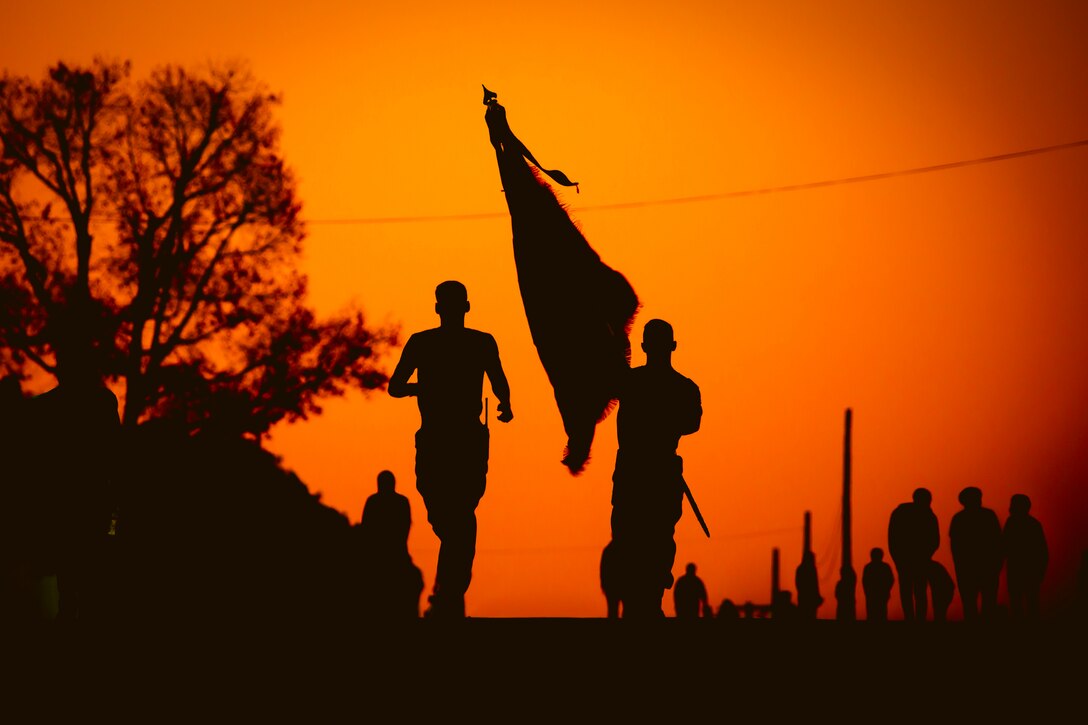 Marines run under a sunlit sky as shown in silhouette.