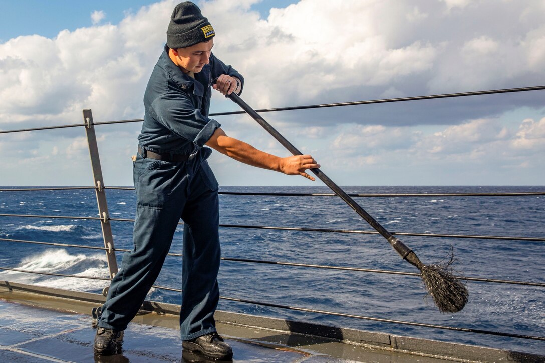 A sailor uses a mop on a ship at sea.