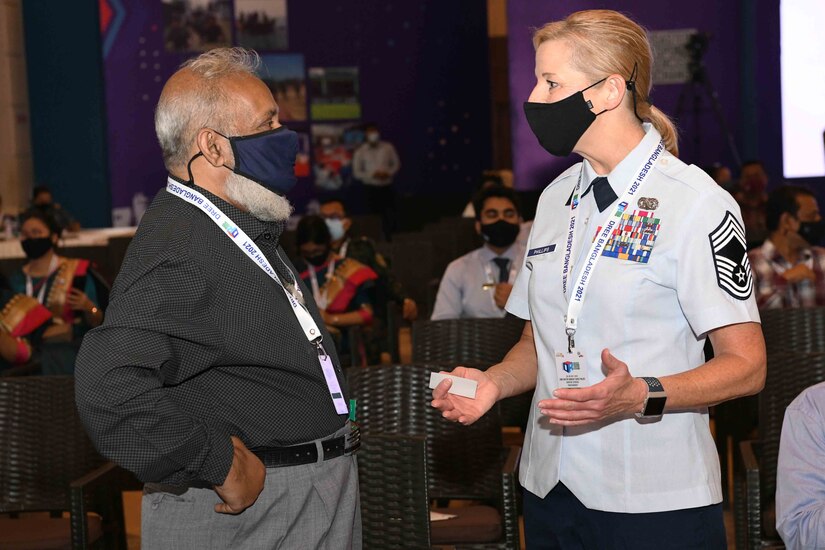 A man and a woman chat with one another; both are wearing face masks.