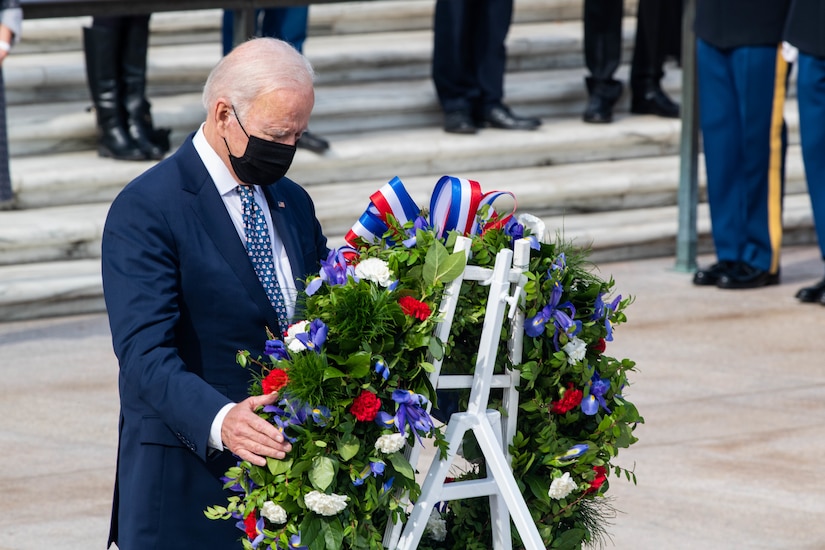 A man stands with his hand on a wreath.